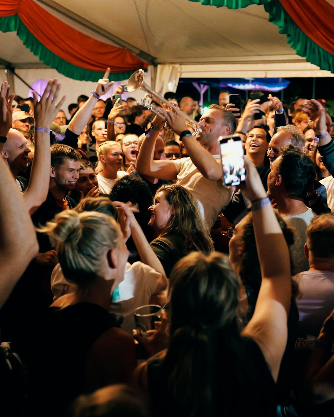 Een muzikant van Orange Brass speelt trompet middenin een feestvierend publiek